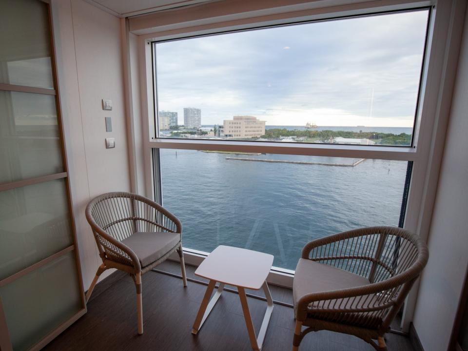 two chairs and a small table in front of a glass wall overlooking the water