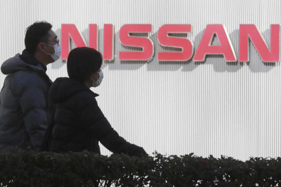 FILE - In this Feb. 9, 2021, file photo, people walk past the corporate logo at Nissan Motor Co.'s global headquarters in Yokohama, near Tokyo. Former Nissan Chief Executive Hiroto Saikawa told a Japanese court Wednesday, Feb. 24, 2021, he believed the compensation for his predecessor Carlos Ghosn was too low “by international standards,” and so he supported Ghosn’s retirement packages to prevent him from leaving. (AP Photo/Koji Sasahara, File)