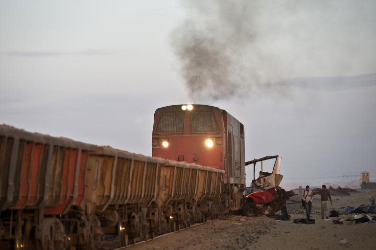 Egyptians walk past the site of an accident near a railway crossing, where a train ploughed into a truck and a mini-bus on November 18, 2013 in Dahshur