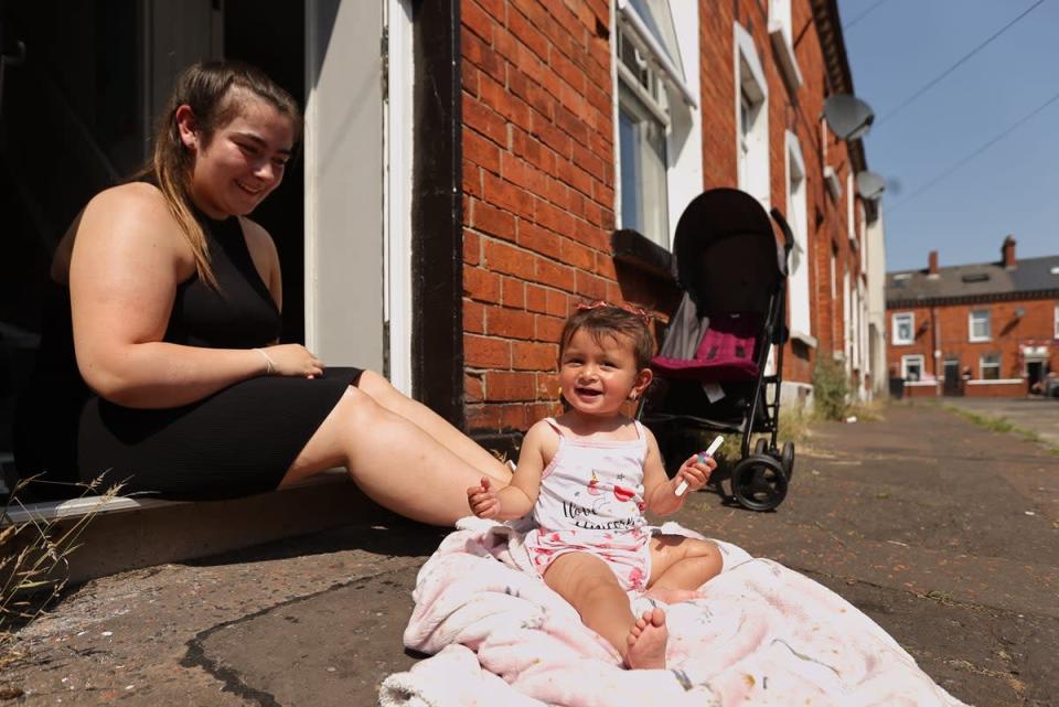 Jasmine Bowers with her daughter Harmony aged one eating a lollipop and enjoying the hot weather outside their home off the Shankill Rd in north Belfast (Liam McBurney/PA) (PA Wire)