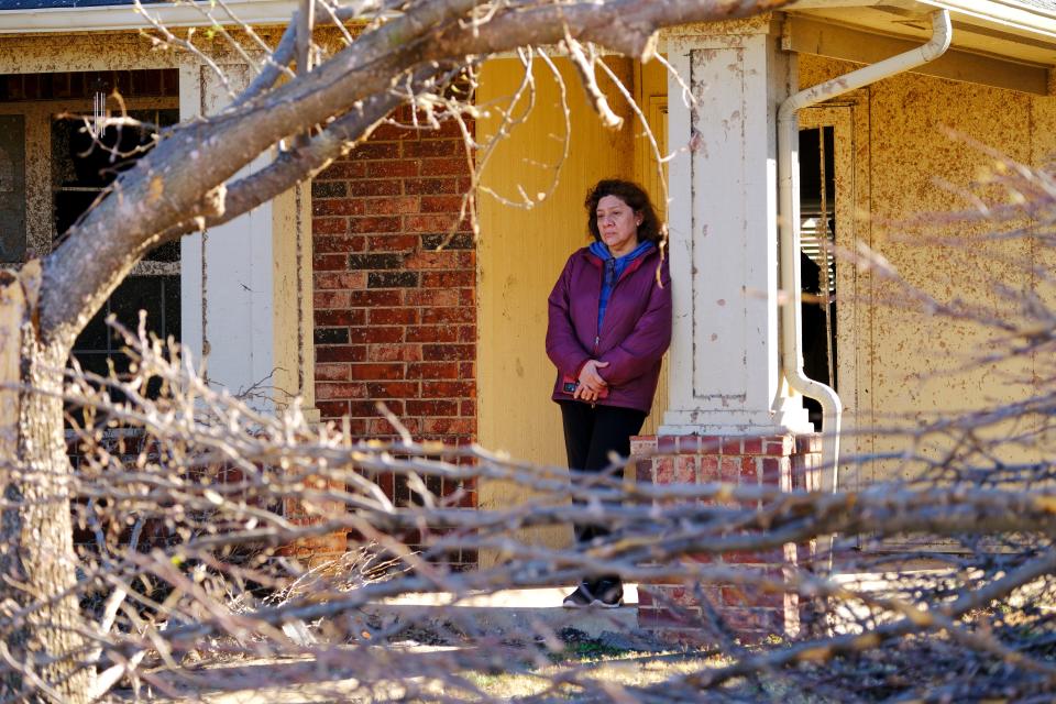 A woman stands Monday by the front door of a house on Conway Drive in the Eastridge neighborhood of Norman. A tornado caused extensive damage Sunday night in Norman.