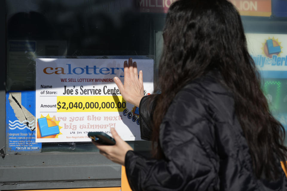 People touch a window sign for good luck announcing the $2.04 billion-winning Powerball ticket award at Joe's Service Center, a Mobil gas station at Woodbury Road and Fair Oaks Avenue in Altadena, Calif., Friday, Jan. 6, 2023. Lottery players whose numbers didn't hit or who forgot to even buy a ticket will have another shot at a nearly $1 billion Mega Millions prize. The estimated $940 million jackpot up for grabs Friday night has been growing for more than two months and now ranks as the sixth-largest in U.S history. (AP Photo/Damian Dovarganes)