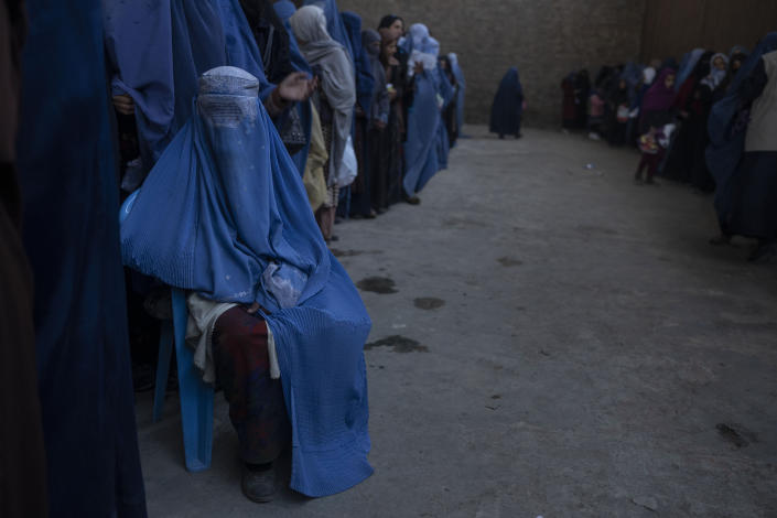 An Afghan woman sits on a chair as she waits with others to receive cash at a money distribution organized by the World Food Program in Kabul, Afghanistan, Saturday, Nov. 20, 2021. With the U.N. warning millions are in near-famine conditions, the WFP has dramatically ramped up direct aid to families. (AP Photo/Petros Giannakouris)