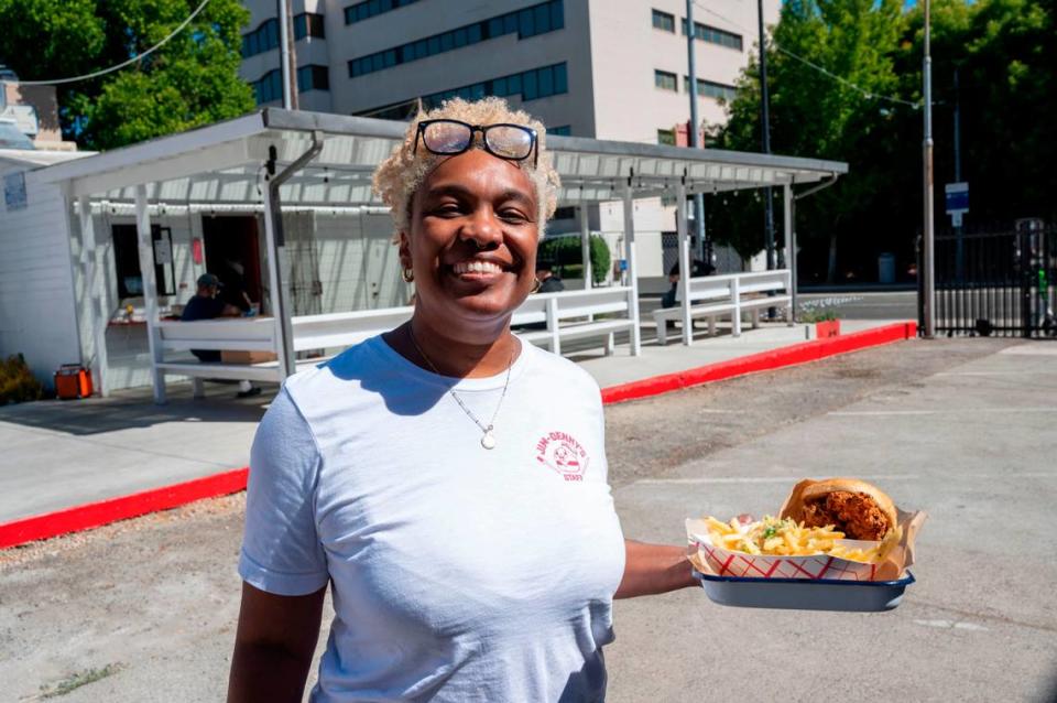 N’Gina Guyton carries out a tempura-battered cod sandwich, served with Havarti cheese and a green goddess tartar sauce on a brioche bun, to a customer sitting outside Jim-Denny’s on Wednesday.