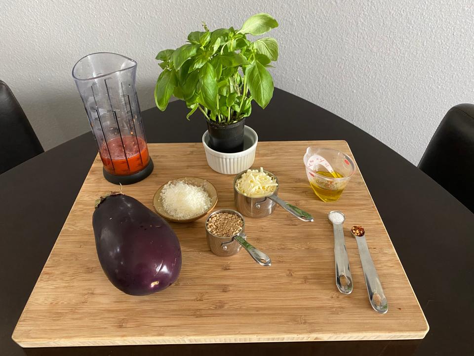 A cutting board covered with ingredients, including basil, eggplant, cheese, salt, red pepper flakes, olive oil, marinara sauce, and breadcrumbs.