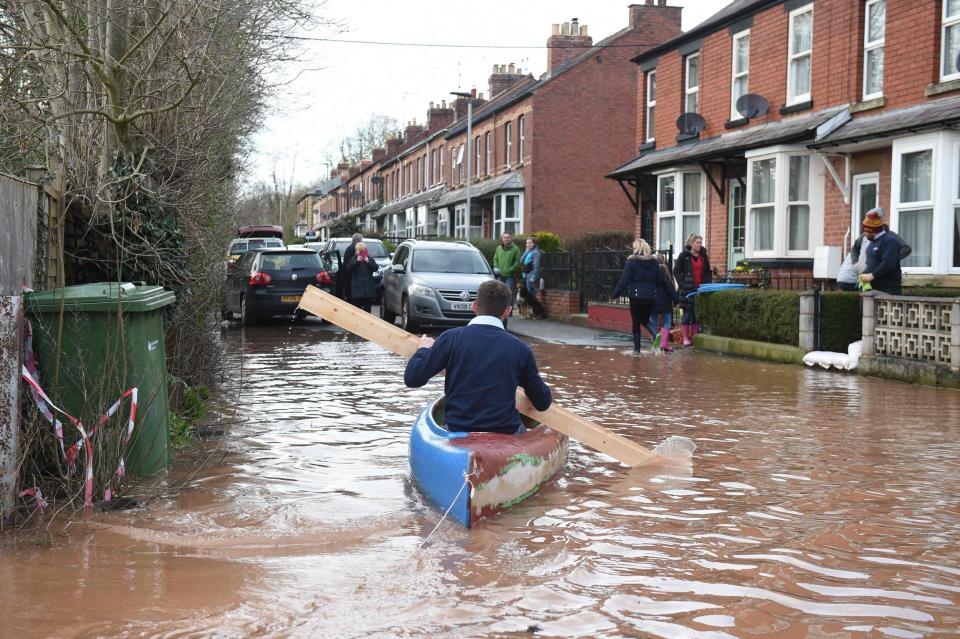 A man uses a plank of wood to paddle a kayak on flood water after the River Wye burst its banks (AFP via Getty Images)