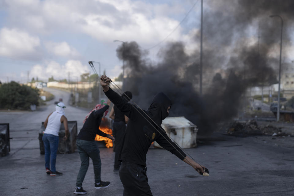 Palestinian protesters use slingshots behind burning tires during clashes with Israeli border police following a protest against Israeli airstrikes on Gaza, in the West Bank city of Ramallah, Wednesday, Oct. 18, 2023. (AP Photo/Nasser Nasser)