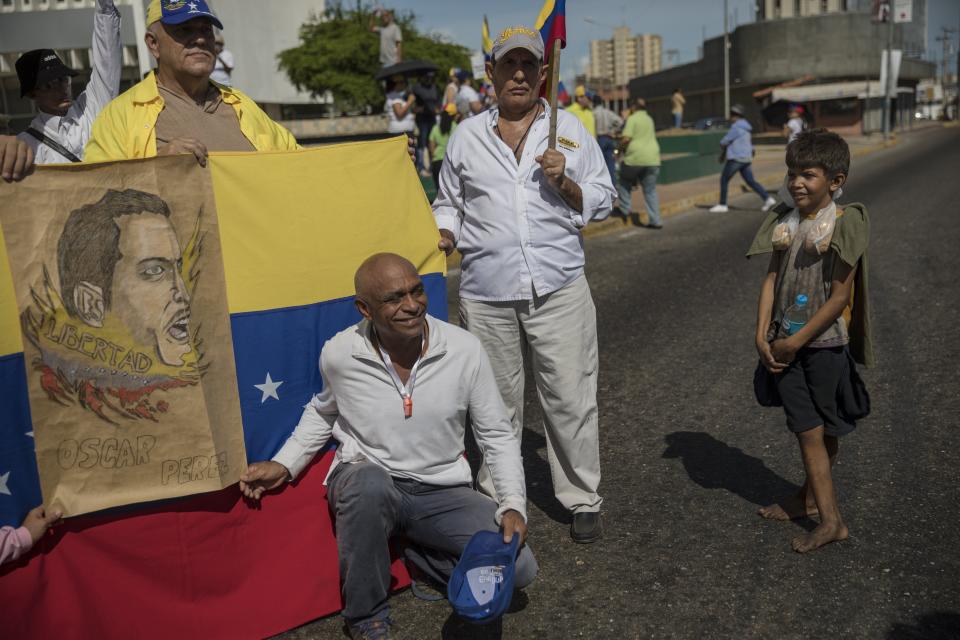 In this Nov. 16, 2019 photo, Oliver Duque, a homeless boy, watches anti-government protestors posing for a picture during a demonstration in Maracaibo, Venezuela. Located in Venezuela’s western Zulia state along the Colombian border, many residents say they’ve abandoned political marches, lacking faith in leaders or fearing for their personal safety. (AP Photo/Rodrigo Abd)