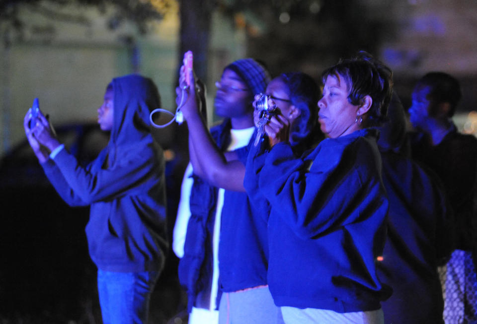 The flashing blue lights of nearby police cars light onlookers trying to capture the scene where authorities say a small plane carrying three people crashed into a home in Jackson, Miss. shortly after 5 p.m. Tuesday evening, Nov. 13, 2012. (AP Photo/The Clarion-Ledger, Joe Ellis) NO SALES
