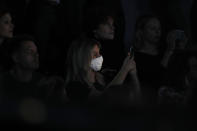 A woman wearing a sanitary mask takes photos during the Dolce & Gabbana women's Fall Winter 2020-21 show, in Milan, Italy, Sunday, Feb. 23, 2020. After Giorgio Armani’s last-minute decision to show his latest collection in an empty theater due to concerns about the new virus, the rest of Milan's runway shows scheduled for Sunday are to go ahead as planned, fashion officials confirmed. (AP Photo/Antonio Calanni)