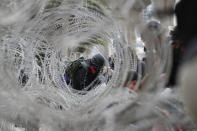 A protester is seen behind rolls of barbed wire barricading the base entrance of the 11th Infantry Regiment, a palace security unit under direct command of the Thai king, Sunday, Nov. 29, 2020, in Bangkok, Thailand. Pro-democracy demonstrators are continuing their protests calling for the government to step down and reforms to the constitution and the monarchy, despite legal charges being filed against them and the possibility of violence from their opponents or a military crackdown. (AP Photo/Sakchai Lalit)