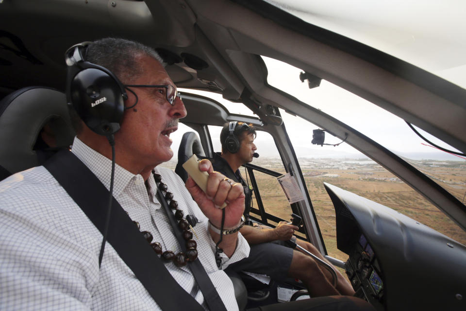 This Thursday, July 11, 2019 photo provided by the County of Maui shows Maui County Mayor Michael Victorino viewing a brush fire that has prompted evacuation orders and diverted flights on the island of Maui in Hawaii. Maui Fire Department officials said hot, dry and windy conditions Friday, July 12, 2019, could worsen the fire. The National Guard is helping firefighters and conducting water drops with a helicopter. The blaze fueled by dry brush and strong winds erupted Thursday on northwestern side of the island, burning 14 square miles (36 square kilometers) of fields. (Chris Sugidono/County of Maui via AP)