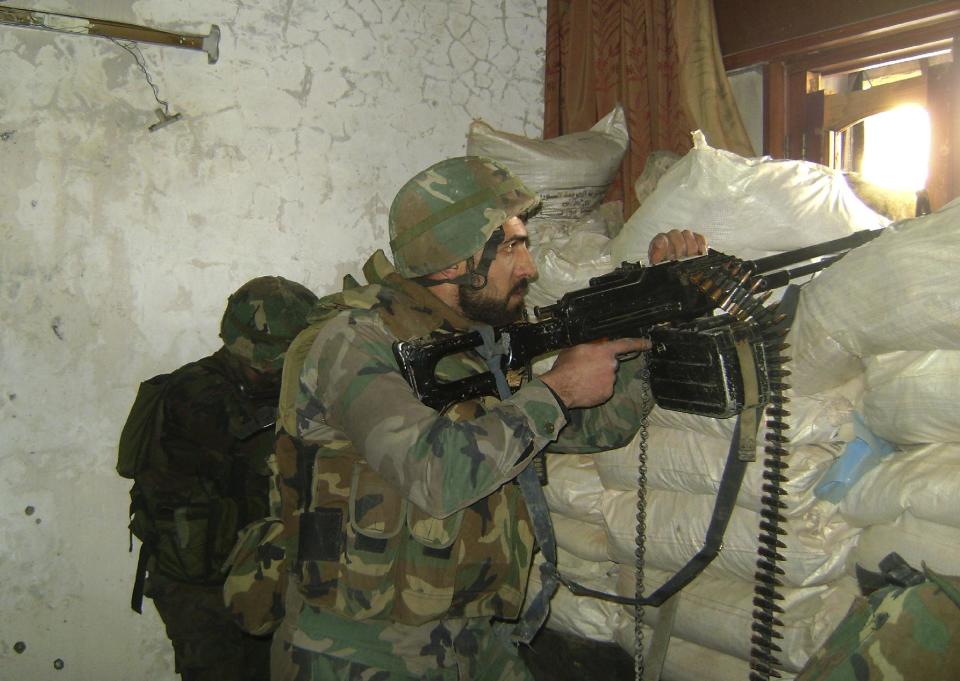 In this photo released by the Syrian official news agency SANA, a Syrian army soldier holds his automatic weapon, as he takes his position behind sand barriers, in the central city of Homs, Syria, Tuesday, Feb. 4, 2014. Since it began with largely peaceful protests in March 2011, the Syrian conflict has killed more than 130,000 people, forced almost a third of the country's prewar population of 23 million from their homes, and inflamed sectarian tensions that have jolted the entire Middle East. (AP Photo/SANA)