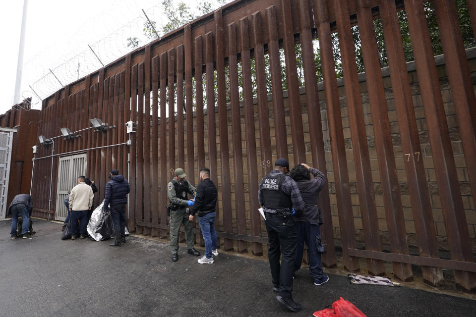 Federal officers remove handcuffs from men before releasing them through a gate in a border wall to Tijuana, Mexico, Wednesday, March 15, 2023, in San Diego. Some asylum-seekers who crossed the border from Mexico are waiting 10 years just for a court date. The Border Patrol released people with notices to appear at a U.S. Immigration and Customs Enforcement office. The move saved the Border Patrol untold hours processing court papers, but it left the job to an agency that had no extra staff for the increased workload. (AP Photo/Gregory Bull)