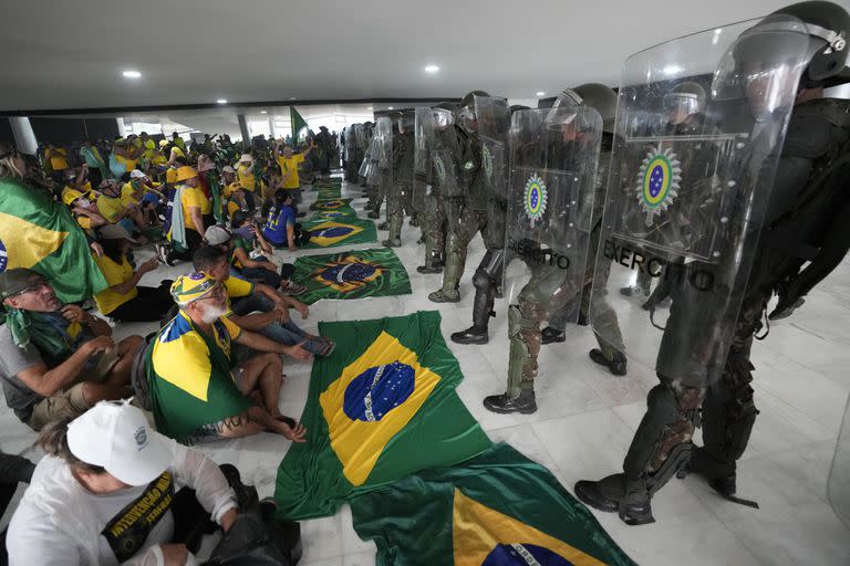 Simpatizantes del expresidente brasileño Jair Bolsonaro permanecen sentados frente a una hilera de policías militares dentro del Palacio de Planalto, luego de irrumpir al interior el domingo 8 de enero de 2023, en Brasilia, Brasil.