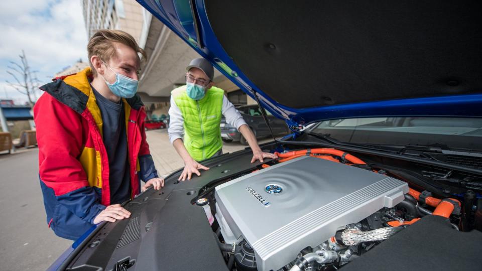 Fahrlehrer Rouven Klein (r) und Fahrschüler Adrian Bredebusch schauen auf die Brennstoffzelle des Wasserstoff-Fahrschulautos der Fahrschule VooVooDrive in Saarbrücken.