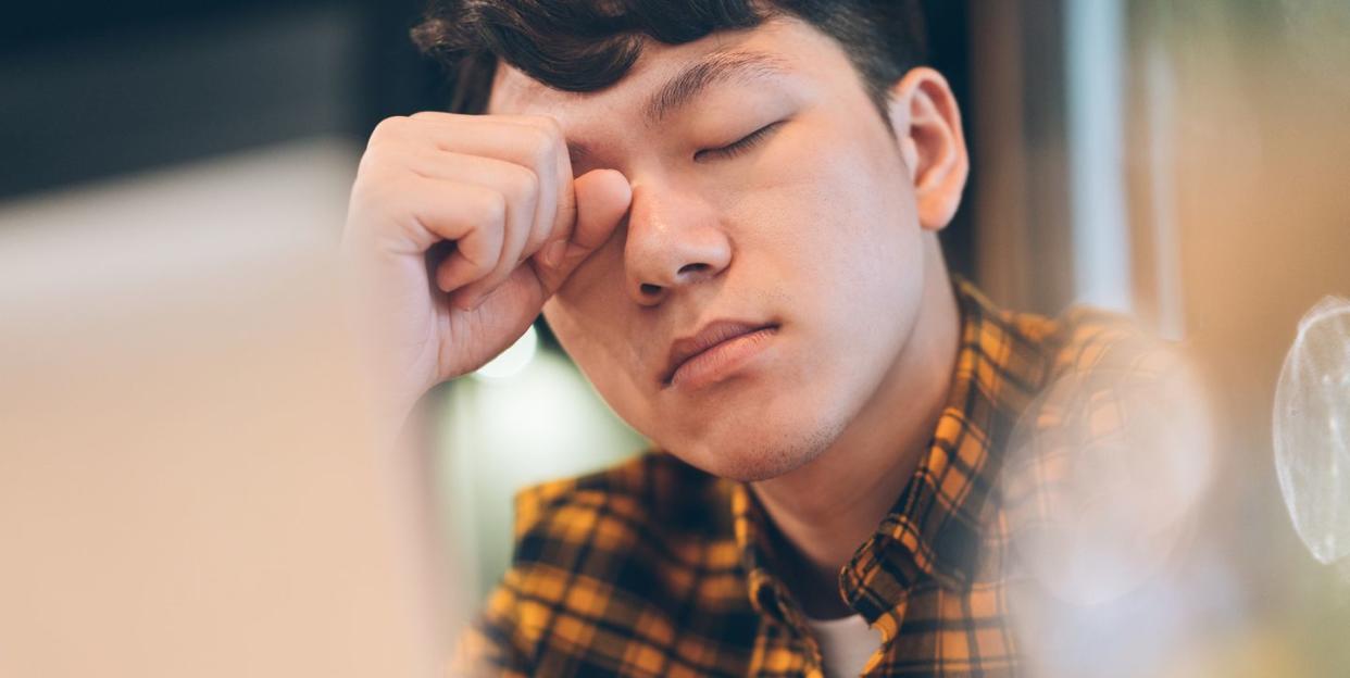 exhausted young man rubbing eyes in cafe