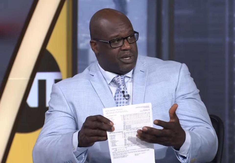 Shaquille O'Neal in a suit holding a piece of paper