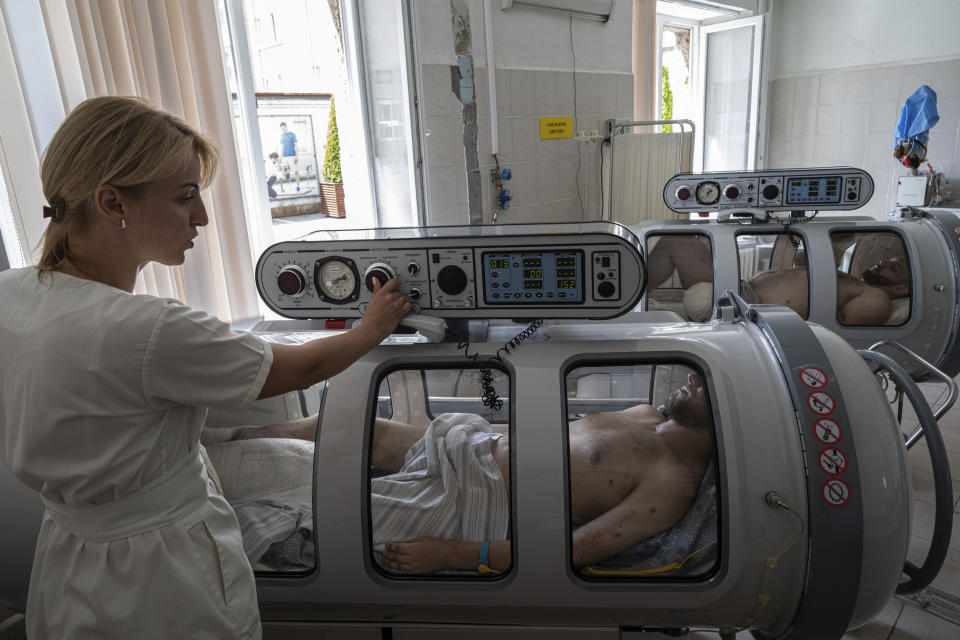 An anaesthesiologist sets up a hyperbaric chamber for Vitaliy Bilyak, a Ukrainian serviceman, during his treatment at St. Panteleimon hospital in Lviv, Ukraine, Tuesday, July 25, 2023. (AP Photo/Evgeniy Maloletka)