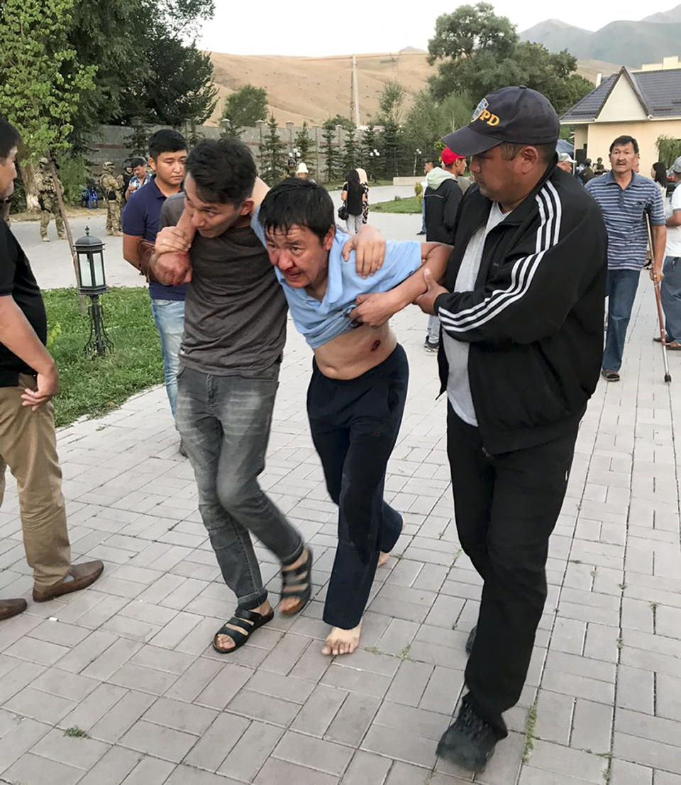 People help a wounded man after shooting at former president of Kyrgyzstan Almazbek Atambayev's residence in the village of Koi-Tash, about 20 kilometers (12 miles) south of the capital, Bishkek, Kyrgyzstan, Wednesday, Aug. 7, 2019. Gunfire is being heard outside the residence of the former president of Kyrgyzstan as police move in to try to arrest him. (AKIpress via AP)