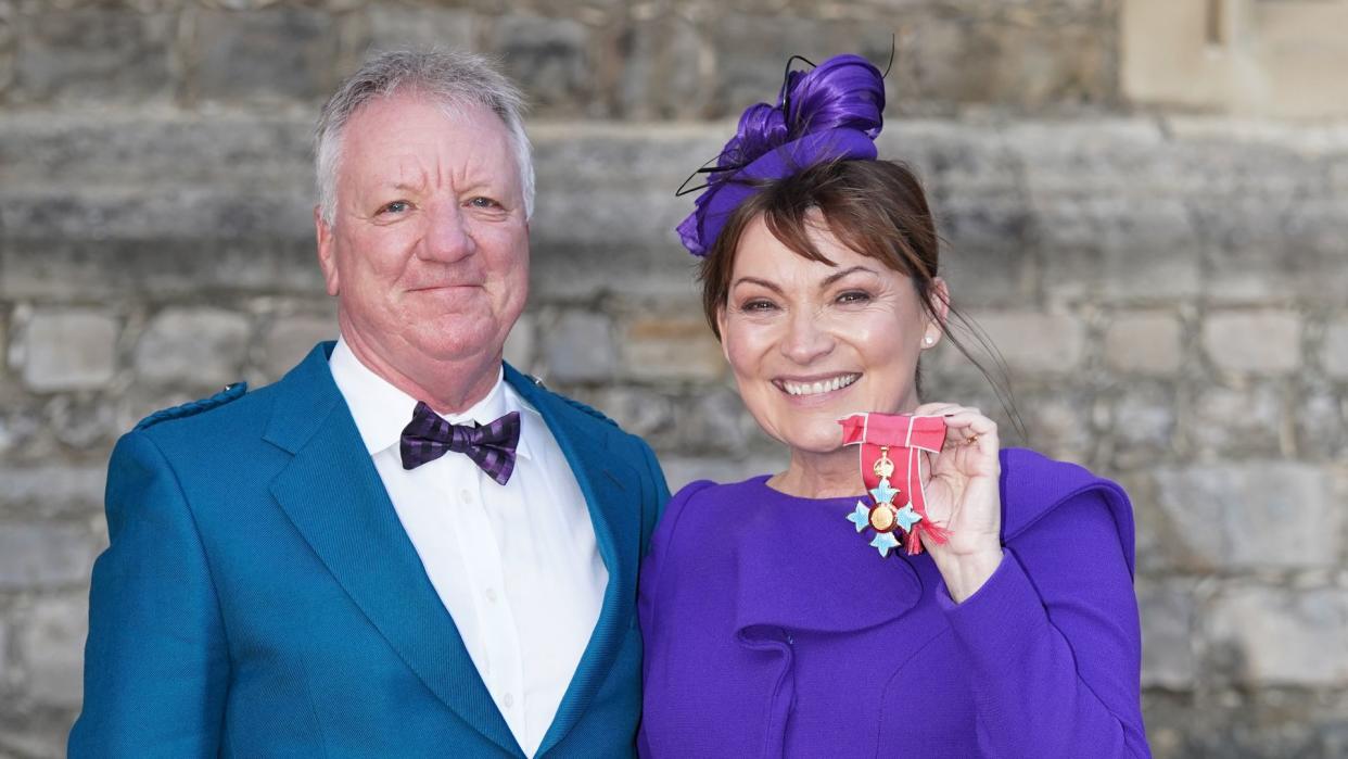 Lorraine Kelly in a purple dress with husband Steve Smith in a blue suit jacket and tartan kilt