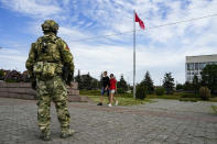 FILE - A young couple walks past a Russian soldier guarding an area at the Alley of Glory exploits of the heroes - natives of the Kherson region, who took part in the liberation of the region from the Nazi invaders, in Kherson, Kherson region, south Ukraine, Friday, May 20, 2022, with a replica of the Victory banner marking the 77th anniversary of the end of World War II right in the background. The Kherson region has been under control of the Russian forces since the early days of the Russian military action in Ukraine. This photo was taken during a trip organized by the Russian Ministry of Defense. (AP Photo, File)