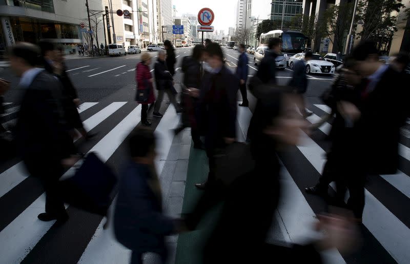 FILE PHOTO: Pedestrians walk past a "no U-turn" traffic sign as they cross a street at a business district in Tokyo