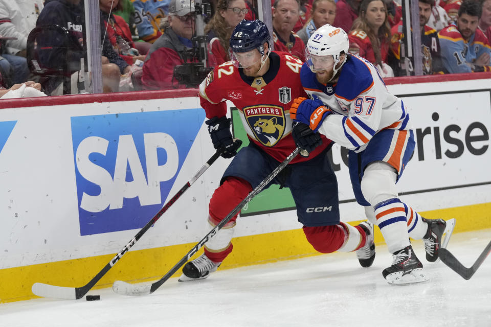 Florida Panthers defenseman Gustav Forsling (42) and Edmonton Oilers center Connor McDavid (97) go after the puck during the third period of Game 5 of the NHL hockey Stanley Cup Finals, Tuesday, June 18, 2024, in Sunrise, Fla. (AP Photo/Wilfredo Lee)