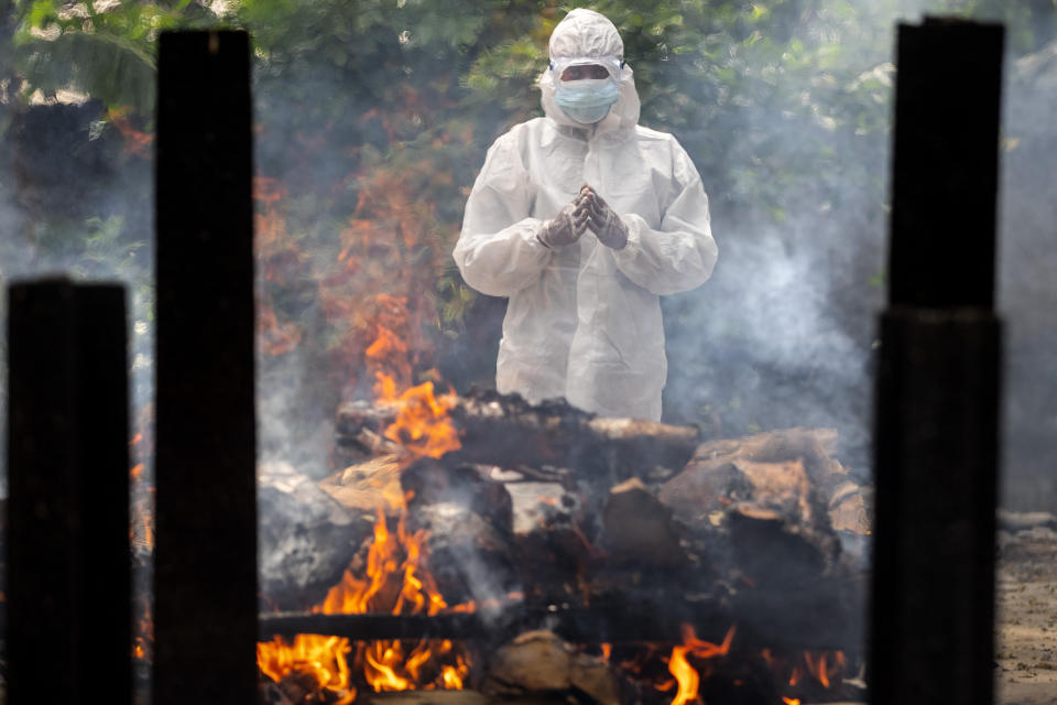 A relative in protective suit performs last rituals near the body of a person who died of COVID-19 during cremation in Gauhati, India, Monday, May 24, 2021. India crossed another grim milestone Monday of more than 300,000 people lost to the coronavirus as a devastating surge of infections appeared to be easing in big cities but was swamping the poorer countryside. (AP Photo/Anupam Nath)