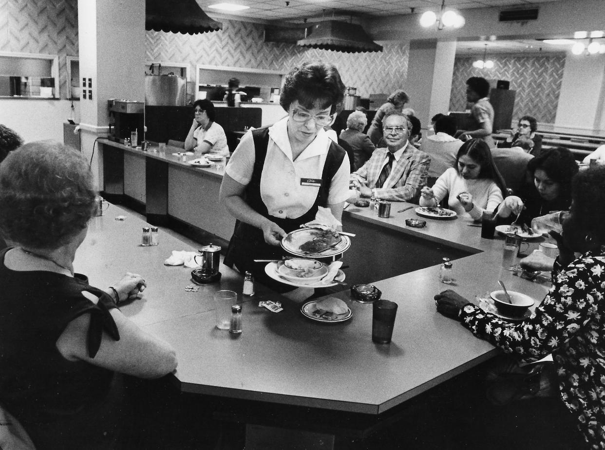 Janet Perry, a 17-year veteran of the Oak Grille, clears dishes May 29, 1984, on the restaurant’s last day at O’Neil’s department store in downtown Akron. Summit County Common Pleas Judge Evan J. Reed, a regular customer, is seated behind her.