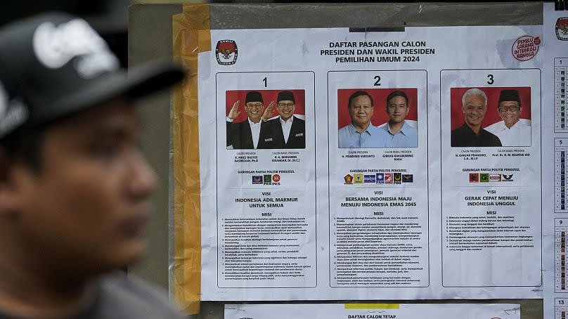 A man walks past a presidential election poster with portraits of presidential candidates