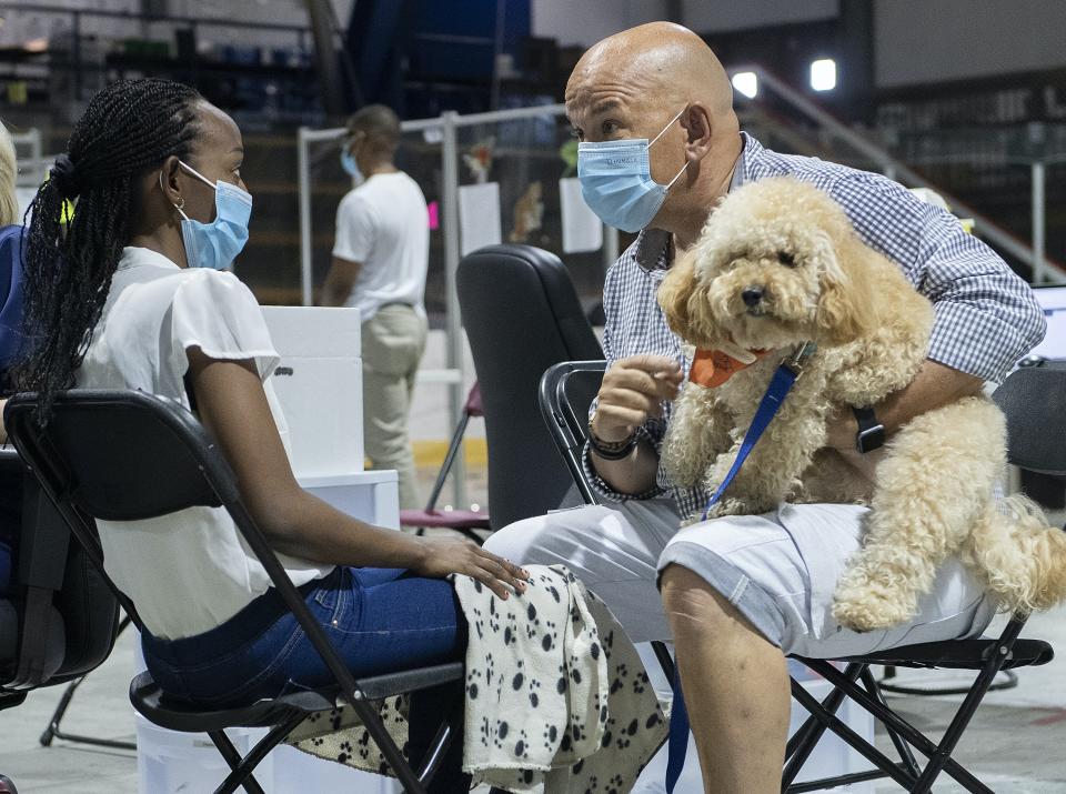 Un homme avec un masque tient un chien devant une jeune femme, portant le masque elle aussi