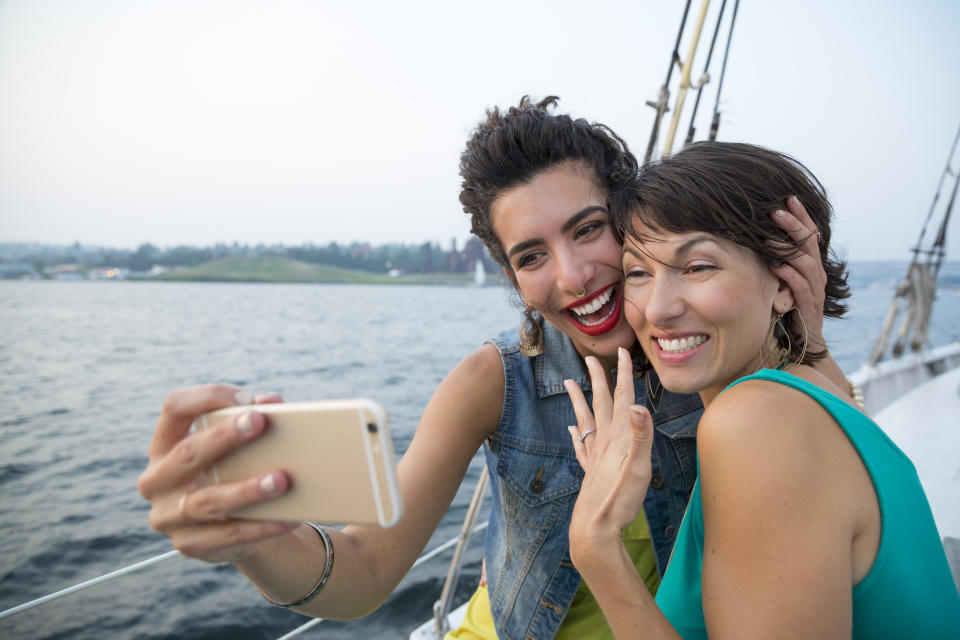 Two woman take an engagement selfie on a sailboat.