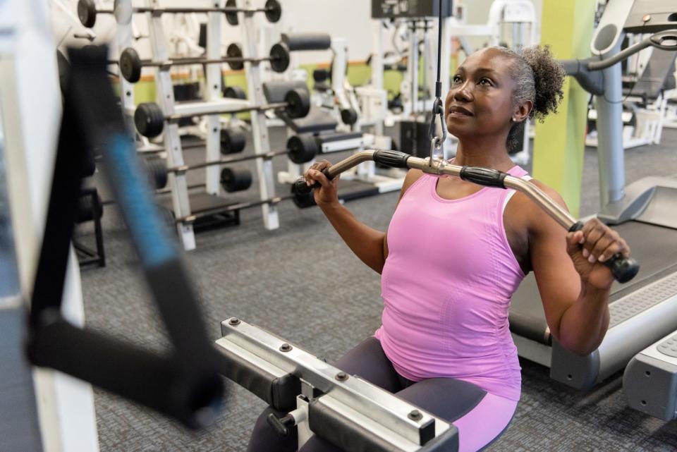 An older woman performing lat pull exercises in the gym on an exercise machine.