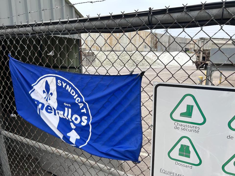 A United Steelworkers flag is hung from the fence of the O-I glass factory in Pointe-Saint-Charles. Behind the fence, hills of broken glass are piled up. 