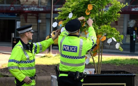 Two police officers stop to read some of the hand-written messages left on one of the 'Trees of Hope"  - Credit: Leon Neal /Getty