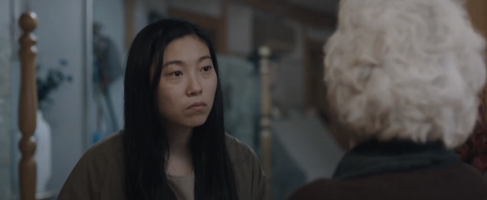 Awkwafina in a scene from a movie, looking at a person with white hair whose back is to the camera