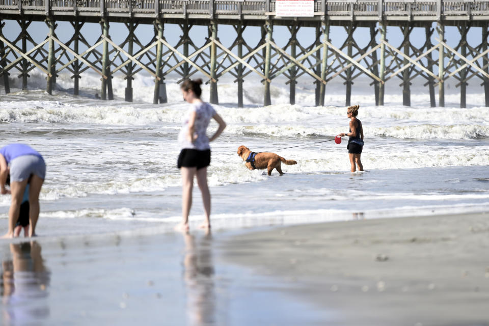 People walk near the pier at Folly Beach, S.C.,, Tuesday, Sept. 3, 2019, ahead of the arrival of Hurricane Dorian. The storm weakened to a Category 2 storm on Tuesday as it continued to batter the Bahamas with life-threatening storm surge. (AP Photo/Meg Kinnard)