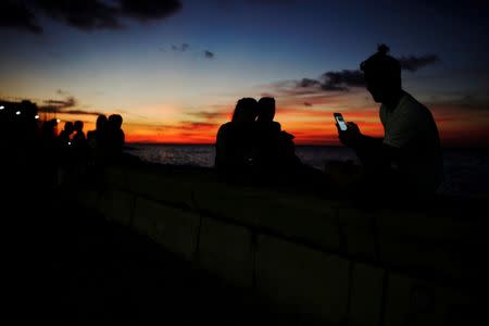 A man chats on the internet with his mobile device during sunset at a hotspot along the seafront in Havana, Cuba, July 14, 2018. REUTERS/Alexandre Meneghini