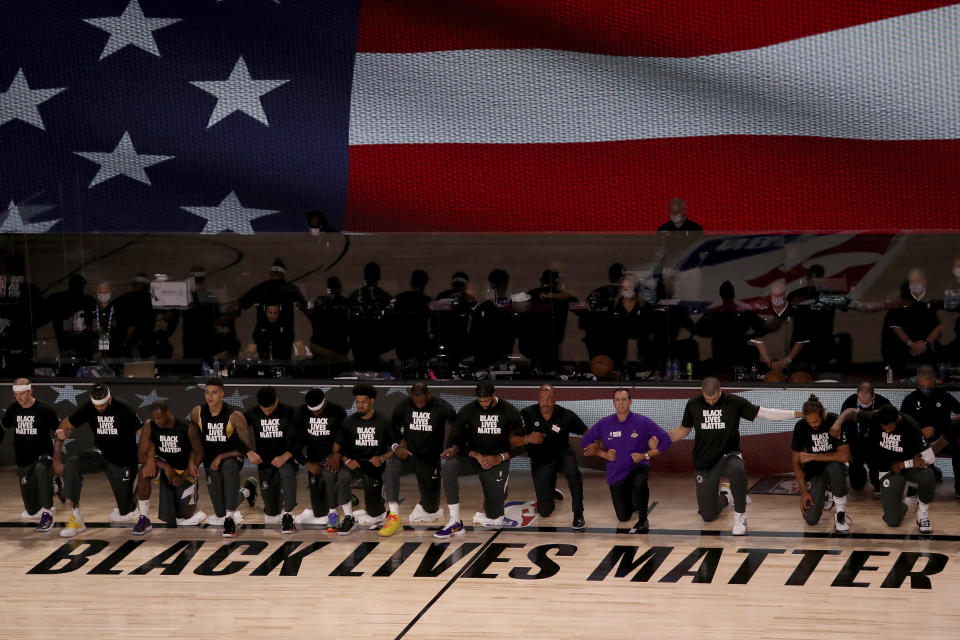 Black Lives Matter written on the court with players kneeling while locking arms and an American flag behind them. 