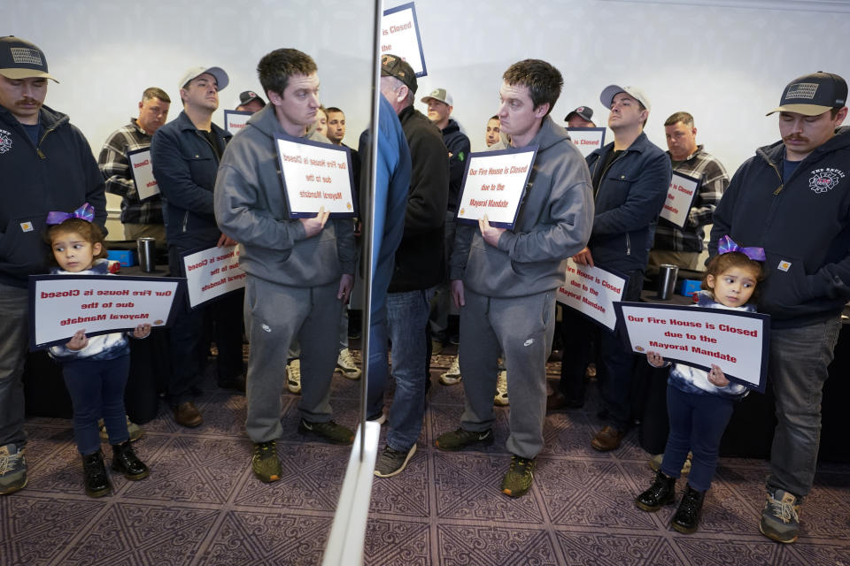 FILE - FDNY firefighters are seen reflected in a mirror holding signs as their union leaders speak during a news conference to protest New York City's COVID-19 vaccine mandate, Tuesday, Nov. 2, 2021, in New York. New York City is ending its COVID-19 vaccination mandate for municipal employees including police officers, firefighters and teachers, Mayor Eric Adams announced Monday, Feb. 6, 2023. The vaccine mandate, which led to the firing of hundreds of city workers who declined to get the shots, will end on Friday, the Democratic mayor said in a news release. (AP Photo/Mary Altaffer, File)