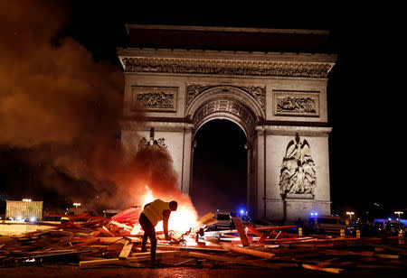 A protester is seen next to a burning barricade during a "Yellow vest" protests against higher fuel prices, on the Champs-Elysees in Paris, France, November 24, 2018. REUTERS/Benoit Tessier