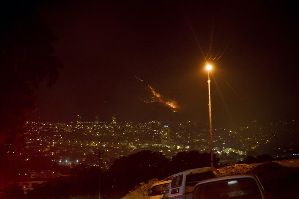 Residential neighborhoods are lit by raging fires in Cape Town, South Africa, Monday, April 19, 2021. Residents are being evacuated from Cape Town neighborhoods after a huge fire spreading on the slopes of the city's famed Table Mountain was fanned by strong winds overnight and threatened houses.(AP Photo/Jerome Delay)