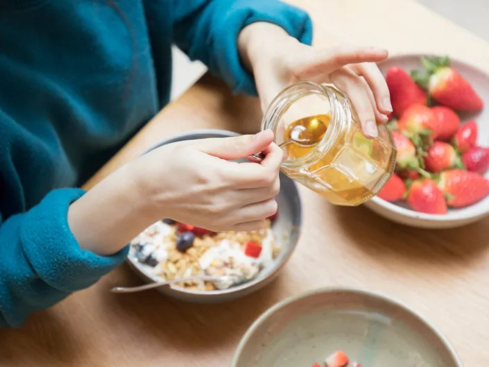 Woman scoops honey from jar with spoon for breakfast.