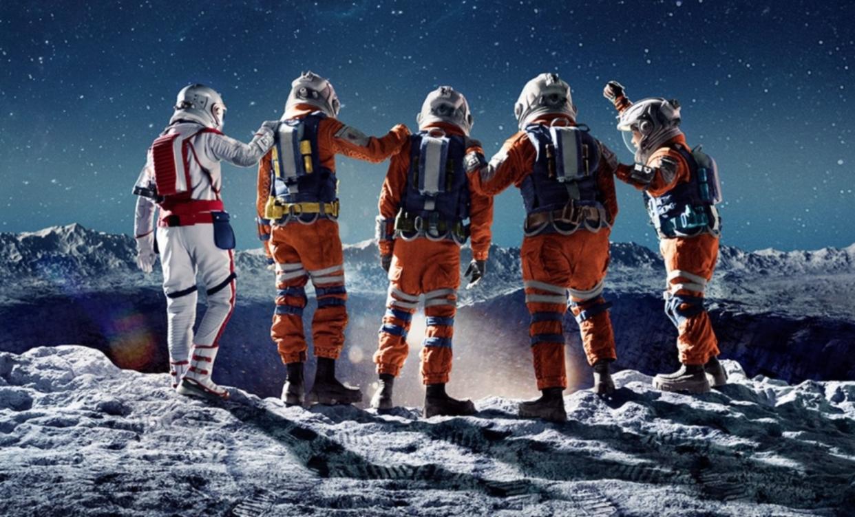  four people in space suits put their arms on one another's shoulders on the surface of the moon while looking down into a large crater 