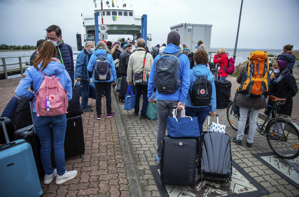 25 May 2020, Mecklenburg-Western Pomerania, Schaprode: Tourists with backpacks and suitcases wait on a pier for transport with a ferry to the Baltic island Hiddensee in Schaprode, Germany, Monday May 25, 2020. In German state Mecklenburg-Western Pomerania, after the travel ban due to the coronavirus protection measures, holidaymakers from other federal states are now allowed to travel to the island. ( Jens Buettner/dpa via AP)