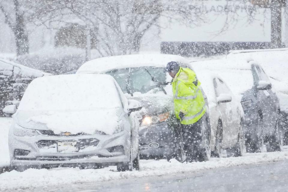 A driver cleans snow off a car in Philadelphia (AP)