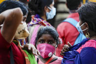 A family wearing face masks to prevent the spread of the coronavirus wait for a bus in Kolkata, India, Friday, Oct. 30, 2020. Health officials have warned about the potential for the coronavirus to spread during the upcoming religious festival season, which is marked by huge gatherings in temples and shopping districts. (AP Photo/Bikas Das)