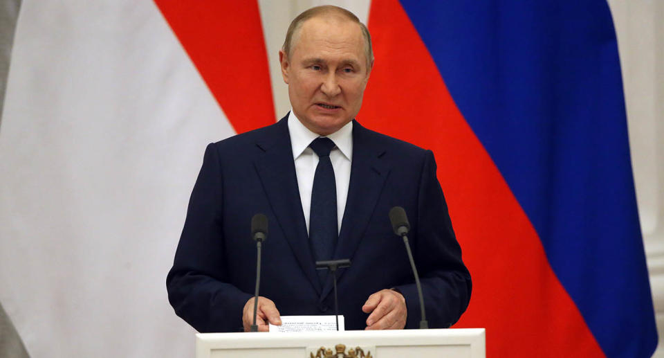 Russian President Vladimir Putin speaks at a lecturn wearing a suit and tie.