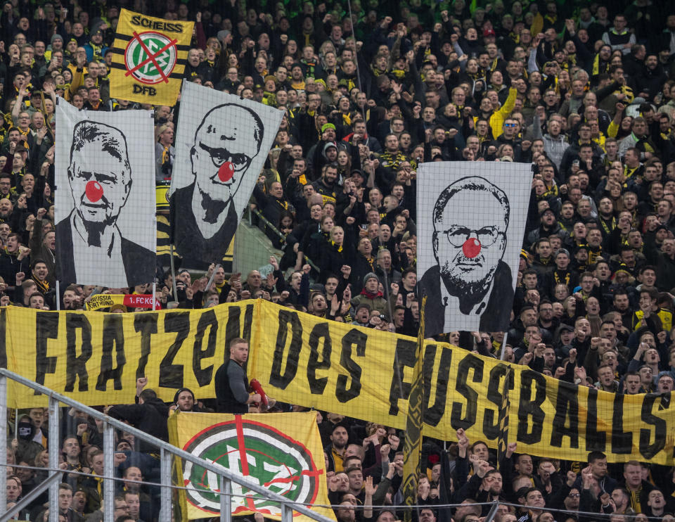 dpatopbilder - 07.03.2020, Nordrhein-Westfalen, Mönchengladbach: Fußball: Bundesliga, Borussia Mönchengladbach - Borussia Dortmund, 25. Spieltag im Borussia Park. BVB-Fans zeigen Banner mit den Gesichtern von Dietmar Hopp (l-r), Fritz Keller und Karl-Heinz Rummenigge mit roter Clownsnase. Darunter ist ein Banner mit der Aufschrift «Die hässlichen Fratzen des Fußball!». Foto: Bernd Thissen/dpa - WICHTIGER HINWEIS: Gemäß den Vorgaben der DFL Deutsche Fußball Liga bzw. des DFB Deutscher Fußball-Bund ist es untersagt, in dem Stadion und/oder vom Spiel angefertigte Fotoaufnahmen in Form von Sequenzbildern und/oder videoähnlichen Fotostrecken zu verwerten bzw. verwerten zu lassen. +++ dpa-Bildfunk +++